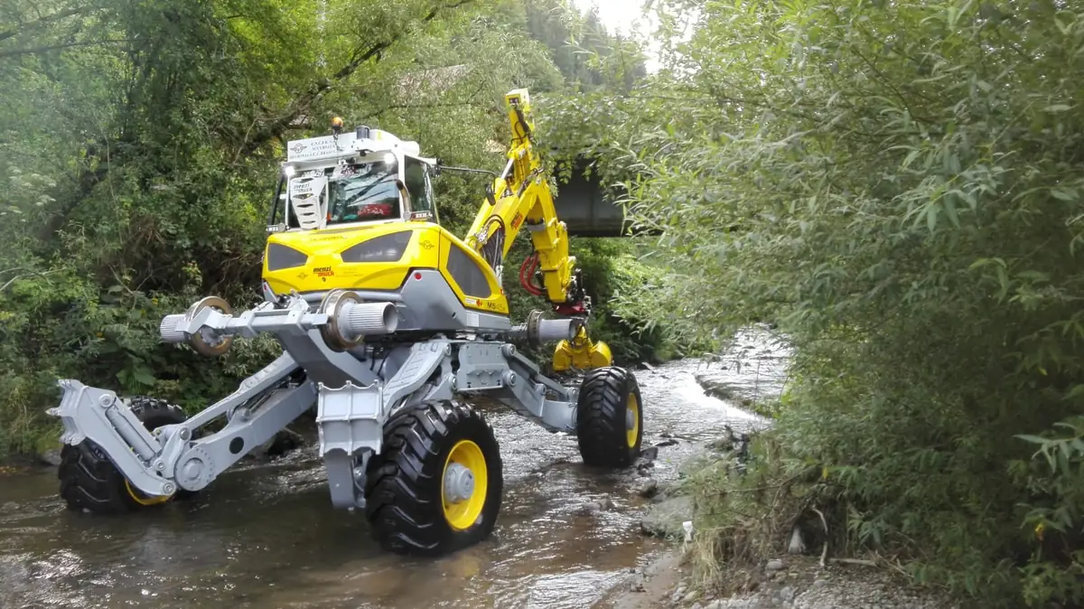 Menzi Muck M545X cu roți de cale ferată, lucrând în albia unui pârâu sub un pod de cale ferată, CFR Brașov