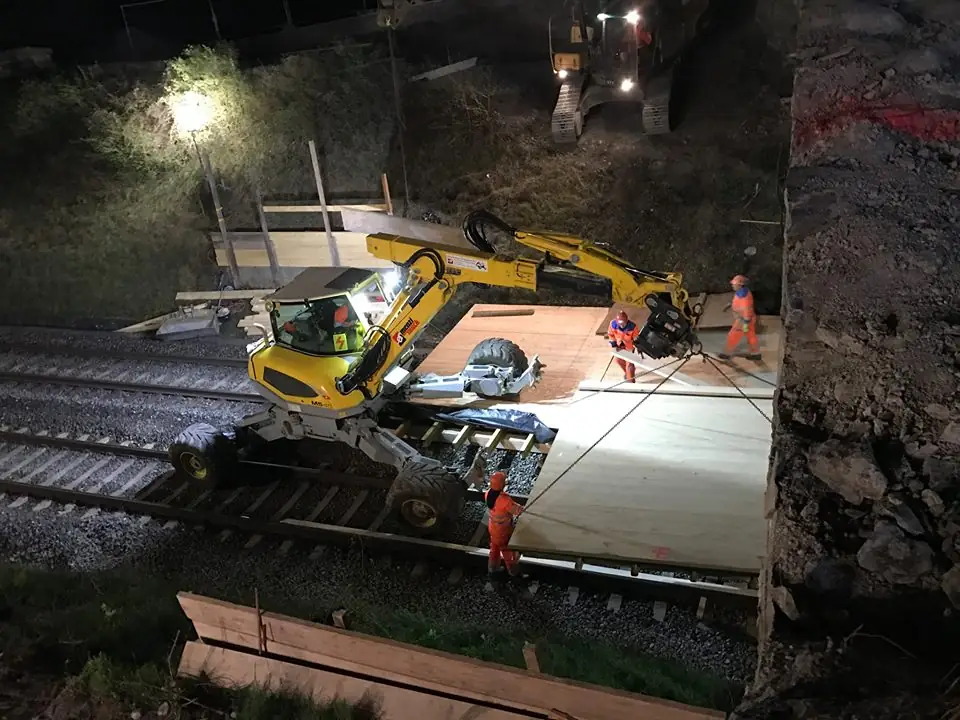 Excavator pășitor Menzi Muck M545 pe șine, lucrând noaptea la ridicarea panourilor de cale ferată