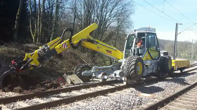 Excavator pășitor cu graifer curățând vegetația de pe taluzul de lângă linia ferată