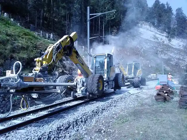 Două Menzi Muck M545 forând pe o linie de munte, în praful de la forare