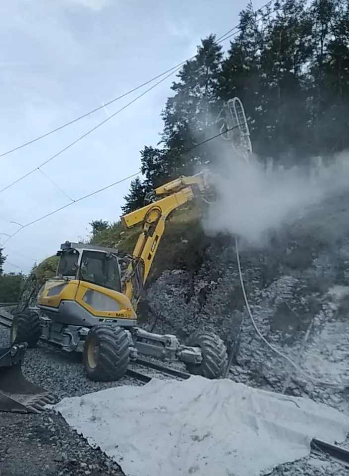 Menzi Muck M545 forând în taluzul de stâncă de lângă calea ferată
