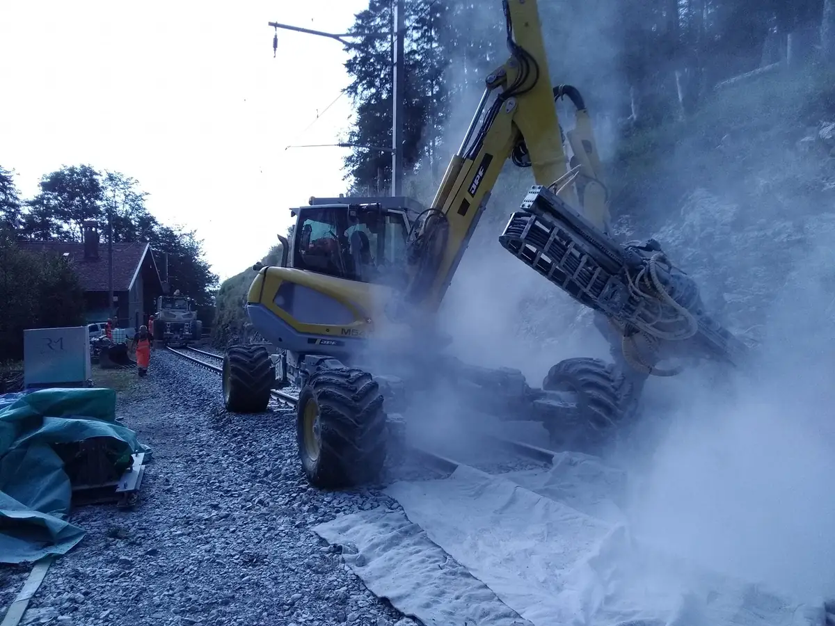Două excavatoare pășitoare pe roți de cale ferată, forând în peretele de stâncă de lângă o linie de munte