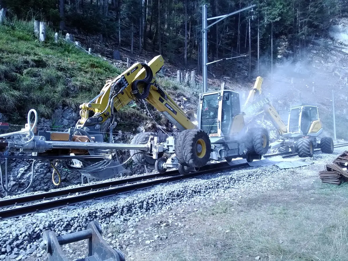 Excavatoare pășitoare cu foreză pe braț, așezate pe șine lângă peretele de stâncă, sub linia de contact