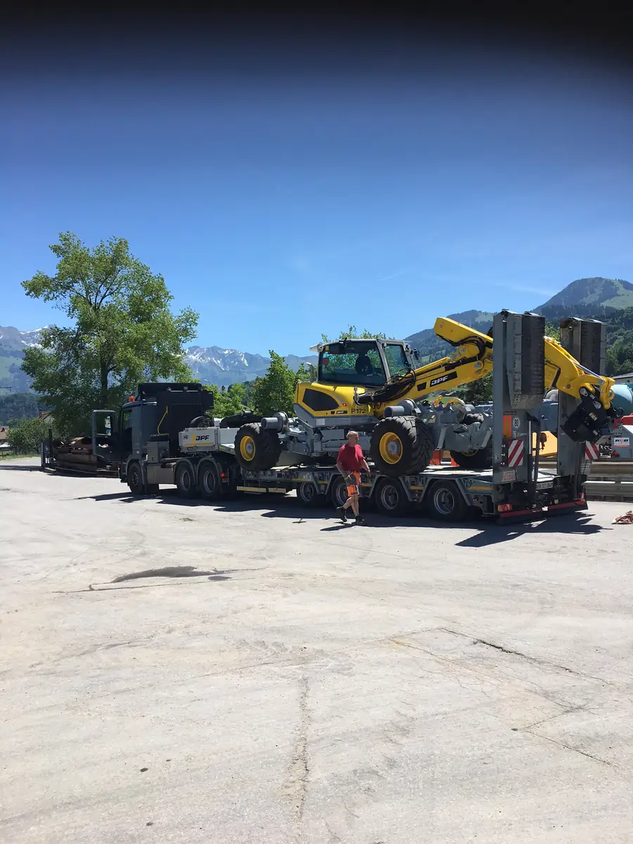 Menzi Muck M545 cu sistem de deplasare pe șine, încărcat pe un trailer cu platformă joasă